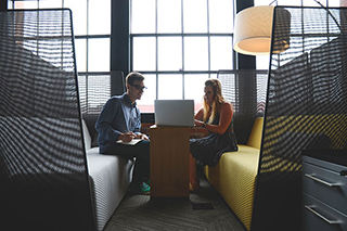 Businessman and woman sitting at a modern booth analyzing their data on a laptop using Minitab statistical software.