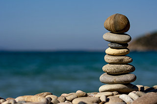 Close up of a rock tower on a rocky  beach with blurred ocean in the background.