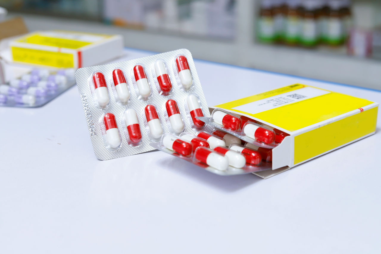 Envases blíster de cápsulas rojas y blancas retiradas parcialmente de una caja con etiqueta amarilla.